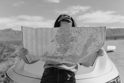 Photo of girl looking at a large map and leaning on car.